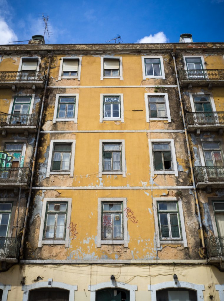687251dca_vertical-shot-old-yellow-painted-apartment-building-with-some-broken-windows